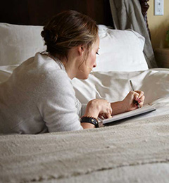 A woman writing in a notepad on her bed