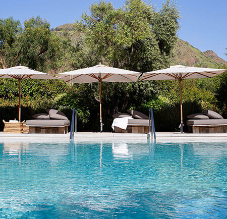 Pool on a sunny day with shade umbrellas and lounge chairs and a view of the mountains