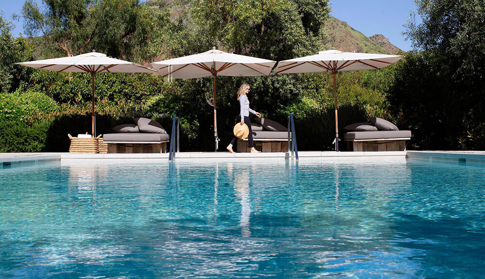 Woman walking beside pool with beige shade umbrellas